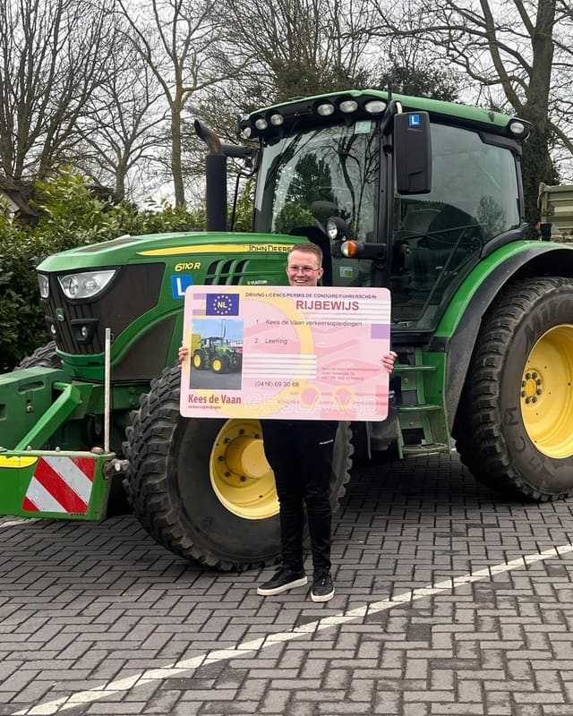 Geslaagde cursist met rijbewijsbord voor een groene lestrekker met aanhangwagen