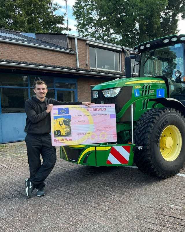 Geslaagd voor het T-rijbewijs: cursist leunt met rijbewijsbord tegen de bumper van een groene lestrekker