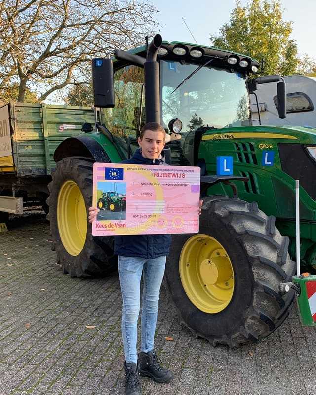Geslaagde cursist in blauwe trui met rijbewijsbord voor een groene lestrekker en kipper
