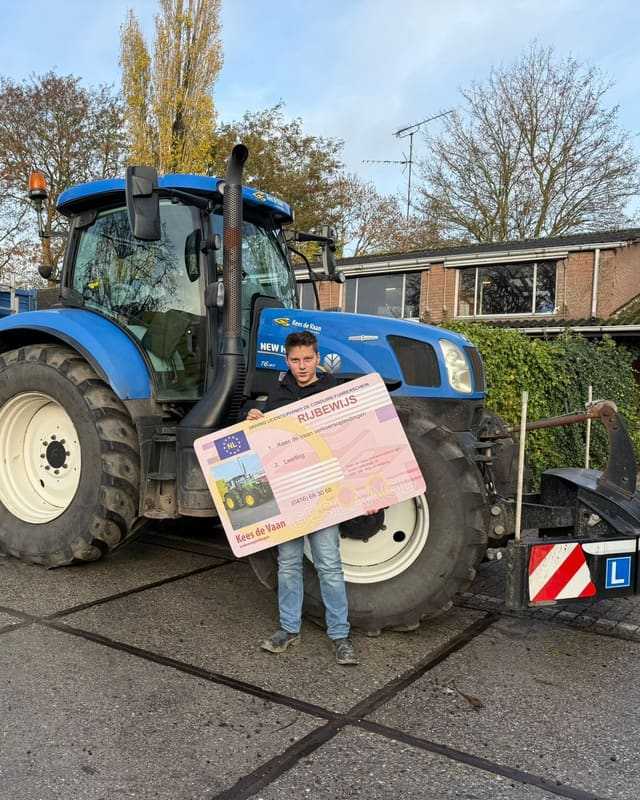 Geslaagde cursist met schuin rijbewijsbord voor een blauwe lestrekker met kipper