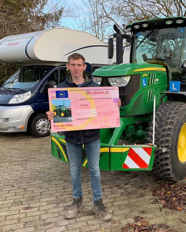 Geslaagd voor het trekkerrijbewijs: cursist met rijbewijsbord voor een groene lestrekker en een camper