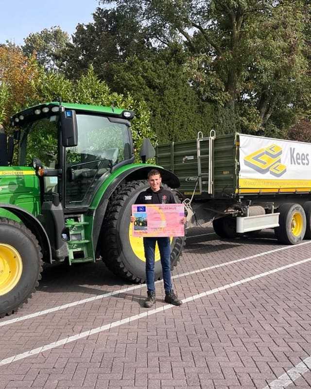 Geslaagde cursist in zwart shirt met rijbewijsbord naast een groene lestrekker met kipper