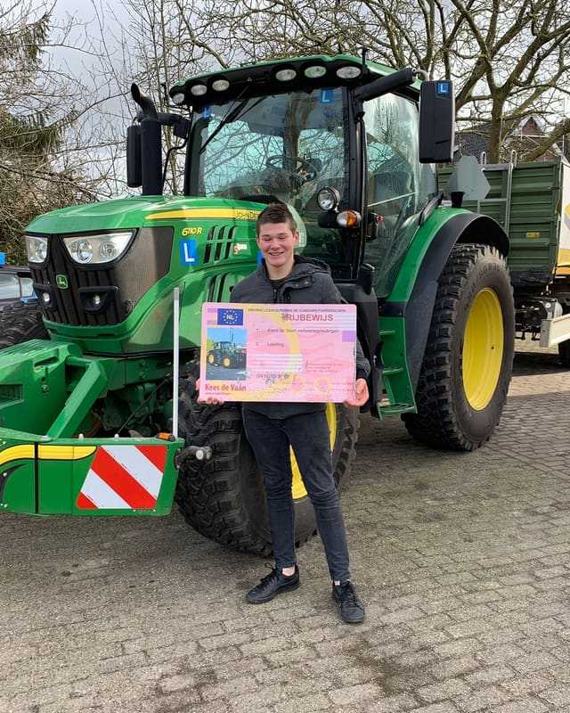 Geslaagd voor het T-rijbewijs: cursist in zwarte jas met rijbewijsbord vlak voor een groene lestrekker