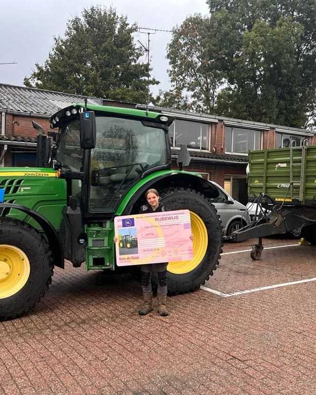 Geslaagde cursist met rijbewijsbord voor het achterwiel van een groene lestrekker