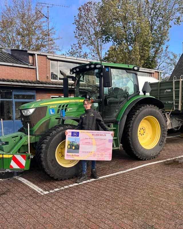 Geslaagd voor het T-rijbewijs: cursist met rijbewijsbord voor het voorwiel van een groene lestrekker