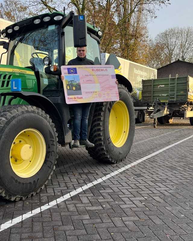 Geslaagde cursist met rijbewijsbord voor de cabine van een groene lestrekker