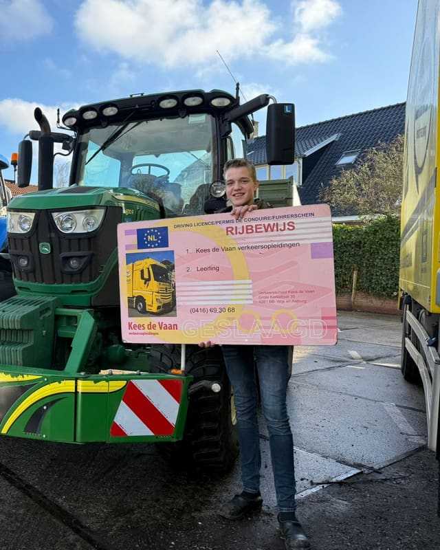 Geslaagd voor het T-rijbewijs: cursist met groot rijbewijsbord naast een groene lestrekker in de winterzon