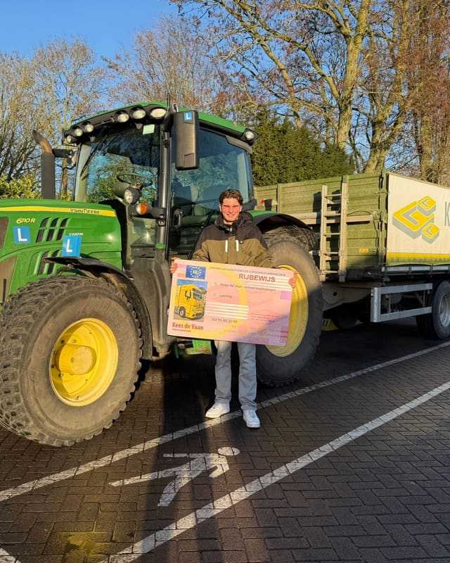 Geslaagd voor het trekkerrijbewijs: cursist met rijbewijsbord voor een groene lestrekker met kipper in de herfst