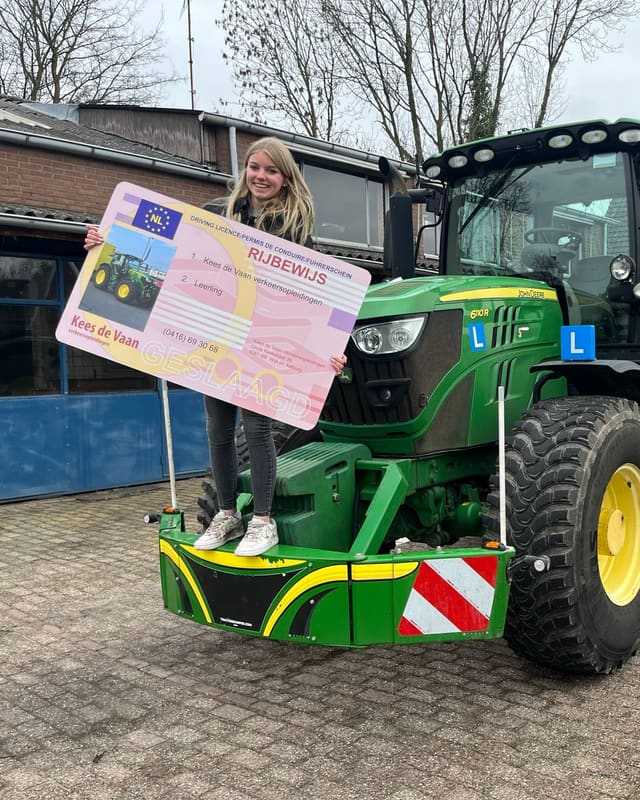 Geslaagd voor het trekkerrijbewijs: cursist houdt het rijbewijsbord omhoog op de bumper van de lestrekker