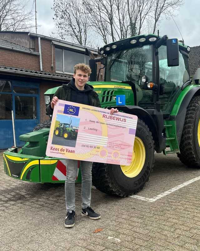 Geslaagd voor het trekkerrijbewijs: cursist met krullen en rijbewijsbord voor een groene lestrekker