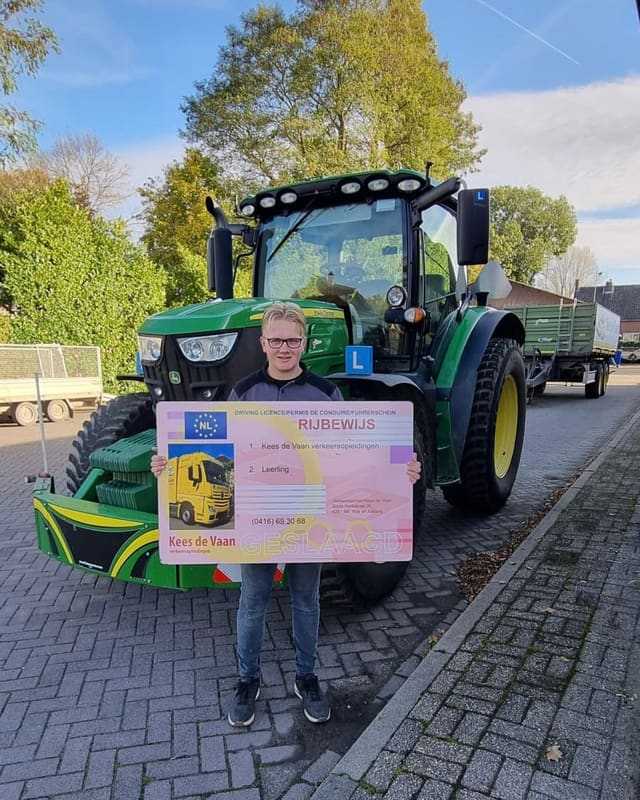Geslaagd voor het trekkerrijbewijs: cursist met rijbewijsbord op de stoep voor een groene lestrekker
