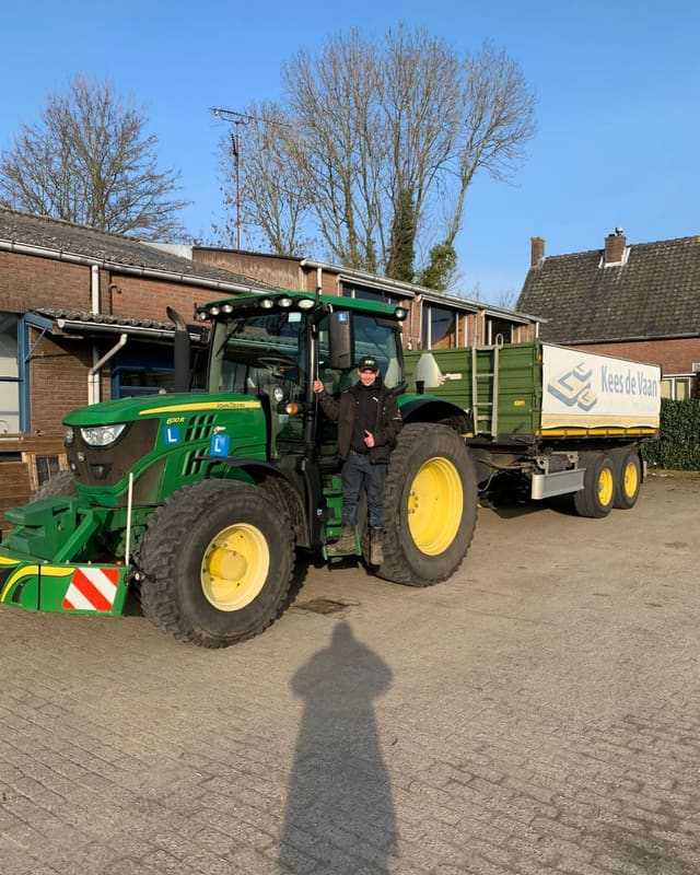 Geslaagde cursist op de opstap van een groene lestrekker met aanhangwagen
