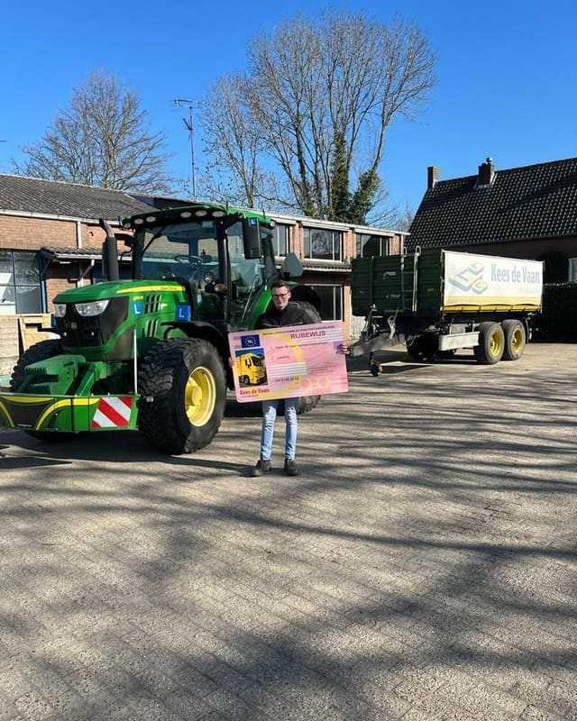 Geslaagd voor het trekkerrijbewijs: cursist met rijbewijsbord op het lesterrein met lestrekker en kipper