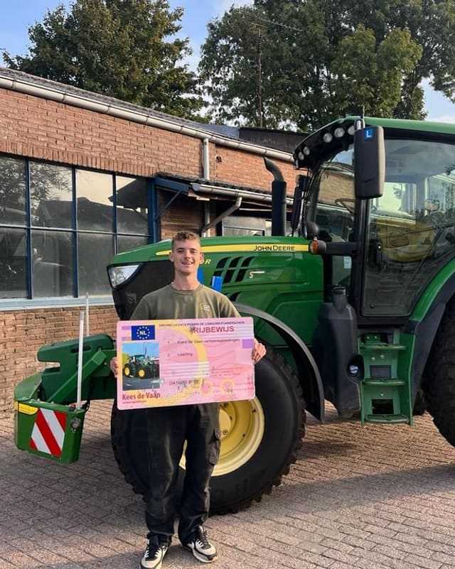 Geslaagde cursist met rijbewijsbord naast een groene lestrekker bij het lesgebouw