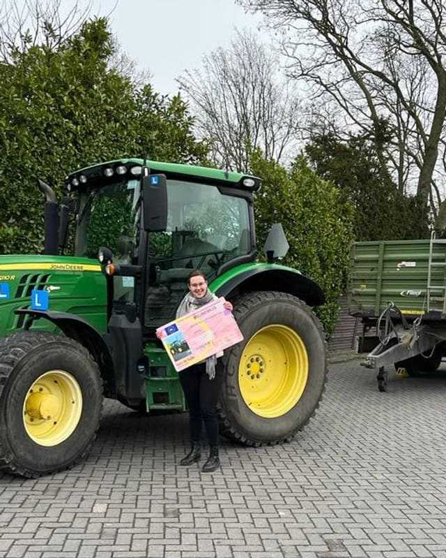 Geslaagde cursist met sjaal en rijbewijsbord bij een groene lestrekker