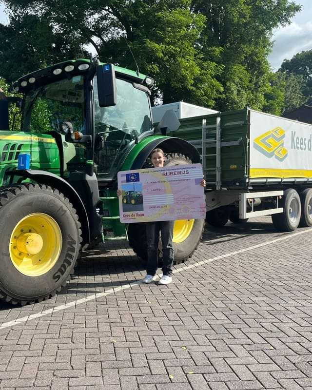 Geslaagd voor het T-rijbewijs: lachende cursist met rijbewijsbord naast de groene lestrekker