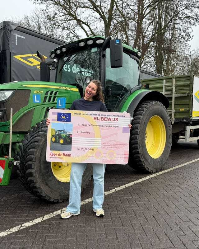 Geslaagde cursist in witte trui met rijbewijsbord voor een groene lestrekker