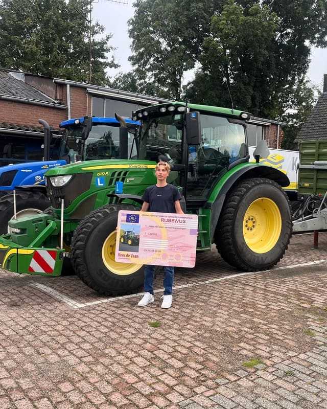Geslaagd voor het trekkerrijbewijs: cursist in zwart T-shirt met rijbewijsbord voor een groene lestrekker