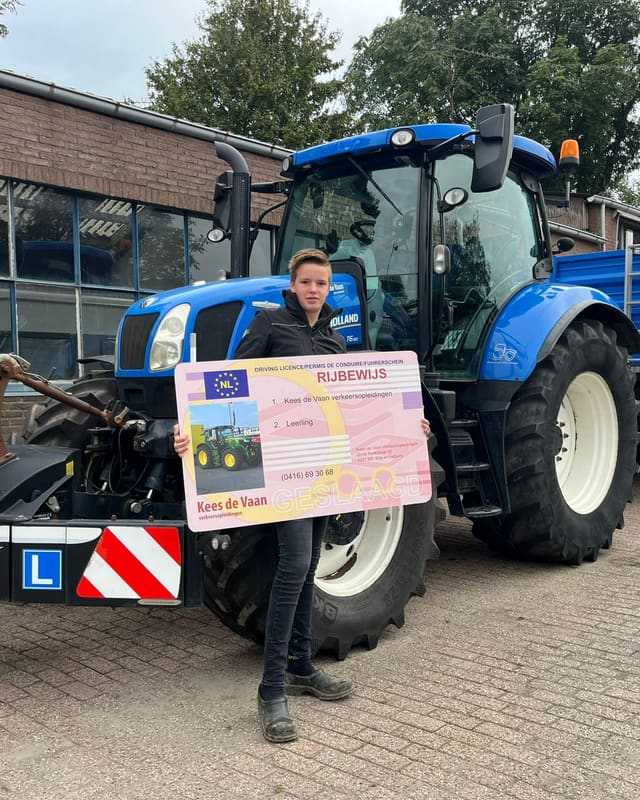 Geslaagd voor het trekkerrijbewijs: cursist met rijbewijsbord voor de bumper van een blauwe lestrekker