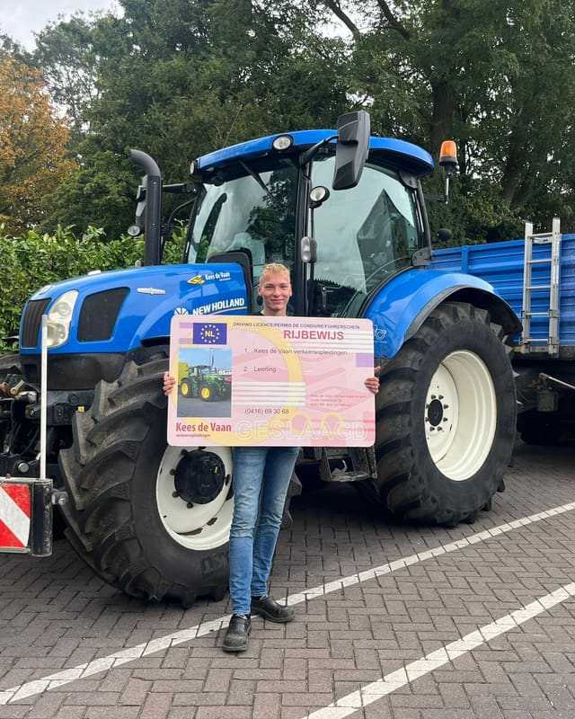 Geslaagd voor het T-rijbewijs: cursist met rijbewijsbord voor een blauwe lestrekker met witte velgen