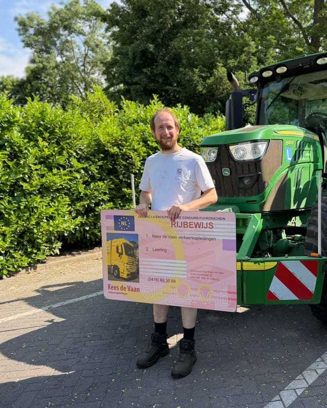 Geslaagde cursist in wit T-shirt met rijbewijsbord voor een groene lestrekker