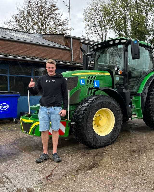 Geslaagd voor het trekkerrijbewijs: cursist in korte broek steekt duim op naast een groene lestrekker