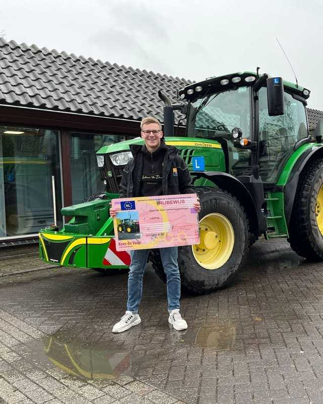 Geslaagd voor het T-rijbewijs: cursist met rijbewijsbord voor een groene lestrekker na een regenbui