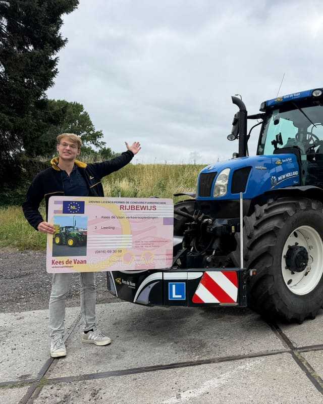 Geslaagd voor het trekkerrijbewijs: cursist met rijbewijsbord wijst naar de blauwe lestrekker