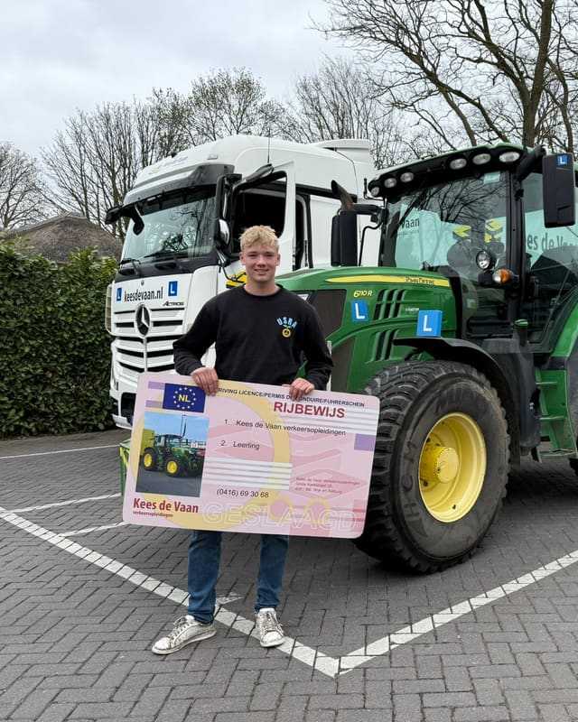 Geslaagd voor het trekkerrijbewijs: cursist met rijbewijsbord voor een groene lestrekker en een witte vrachtwagen