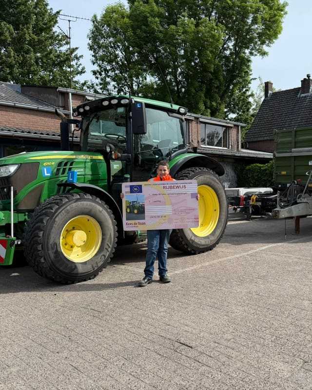 Geslaagd voor het trekkerrijbewijs: cursist in oranje shirt met rijbewijsbord voor een groene lestrekker