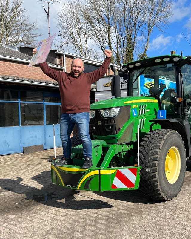 Geslaagde cursist juicht met het rijbewijsbord op de bumper van de lestrekker