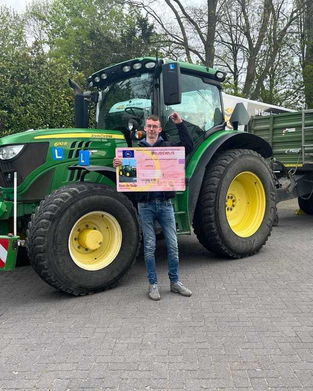 Geslaagd voor het T-rijbewijs: cursist met rijbewijsbord voor een groene lestrekker met kipper in de schaduw
