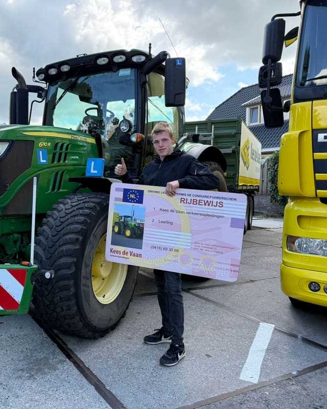 Geslaagd voor het trekkerrijbewijs: cursist met rijbewijsbord tussen een groene lestrekker en een gele lesvrachtwagen
